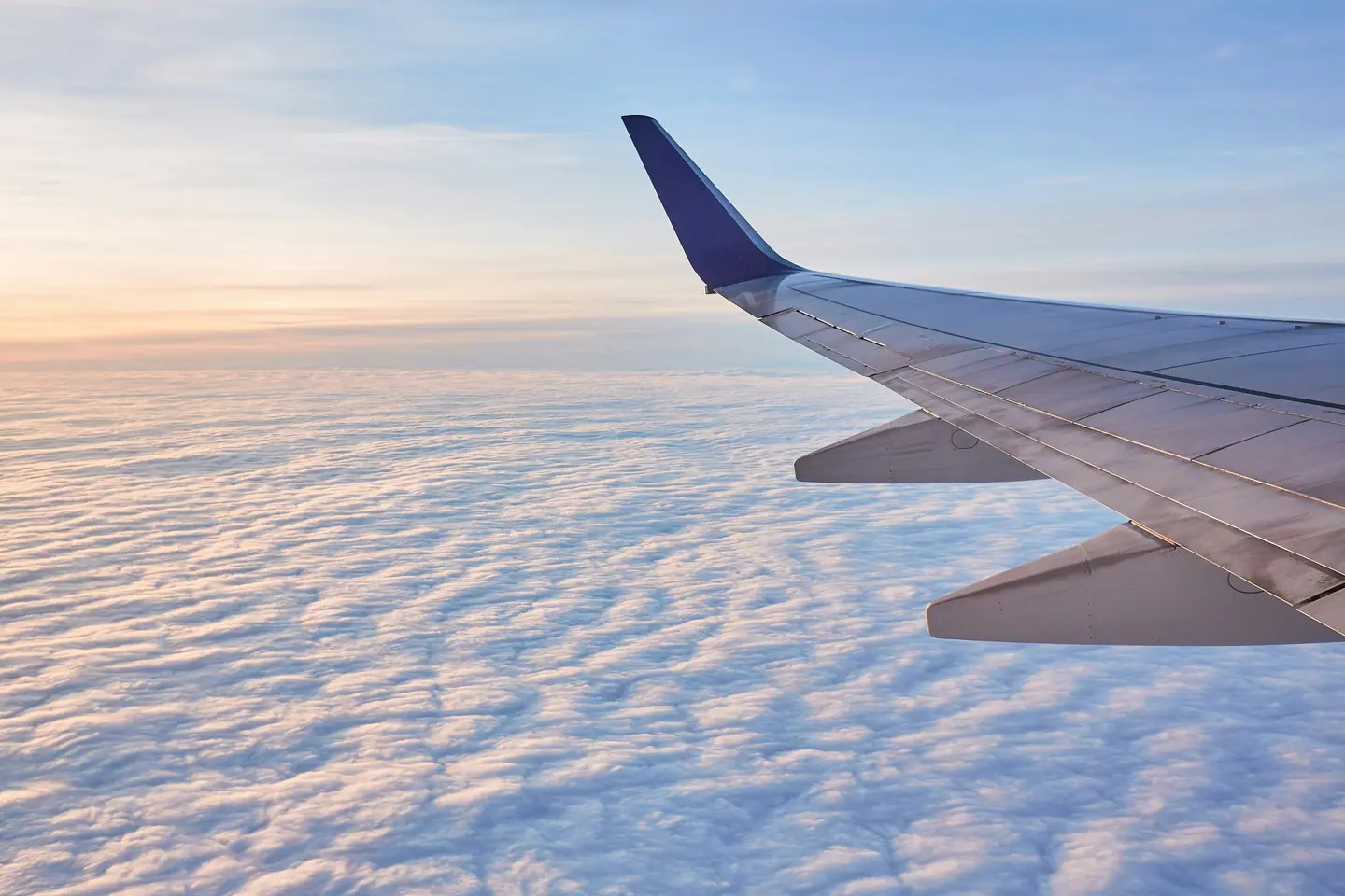 Ala de un avión sobre un mar de nubes teñidas de rosa al amanecer