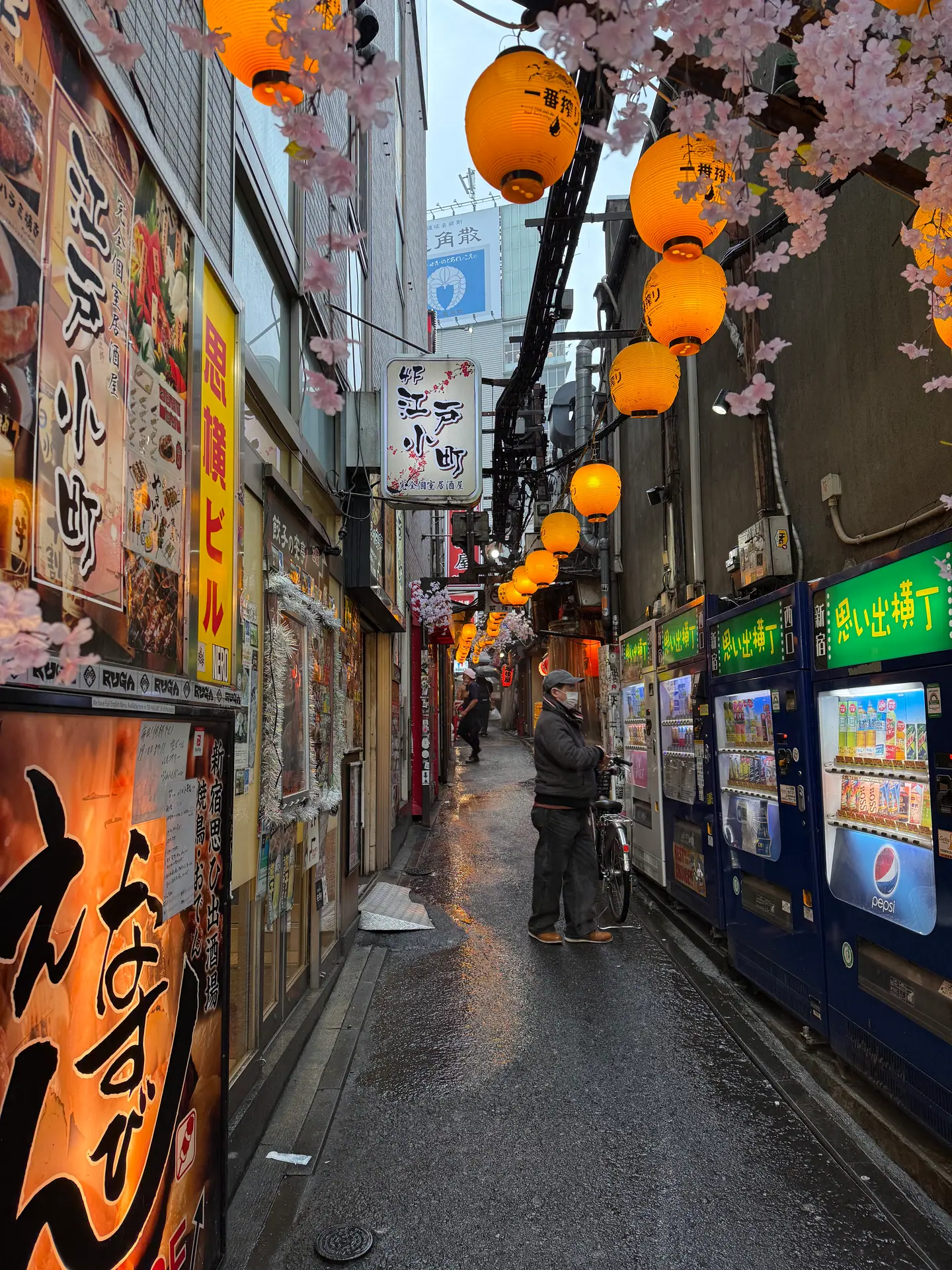 Callejón estrecho de Omoide Yokocho con farolillos amarillos, flores de cerezo decorativas y máquinas expendedoras, Shinjuku, Tokio