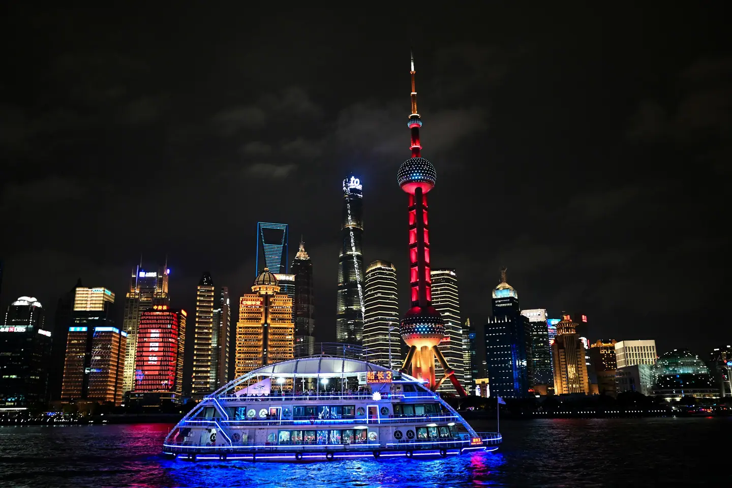 Barco iluminado navegando de noche por el río Huangpu ante los rascacielos de Pudong, en Shanghái