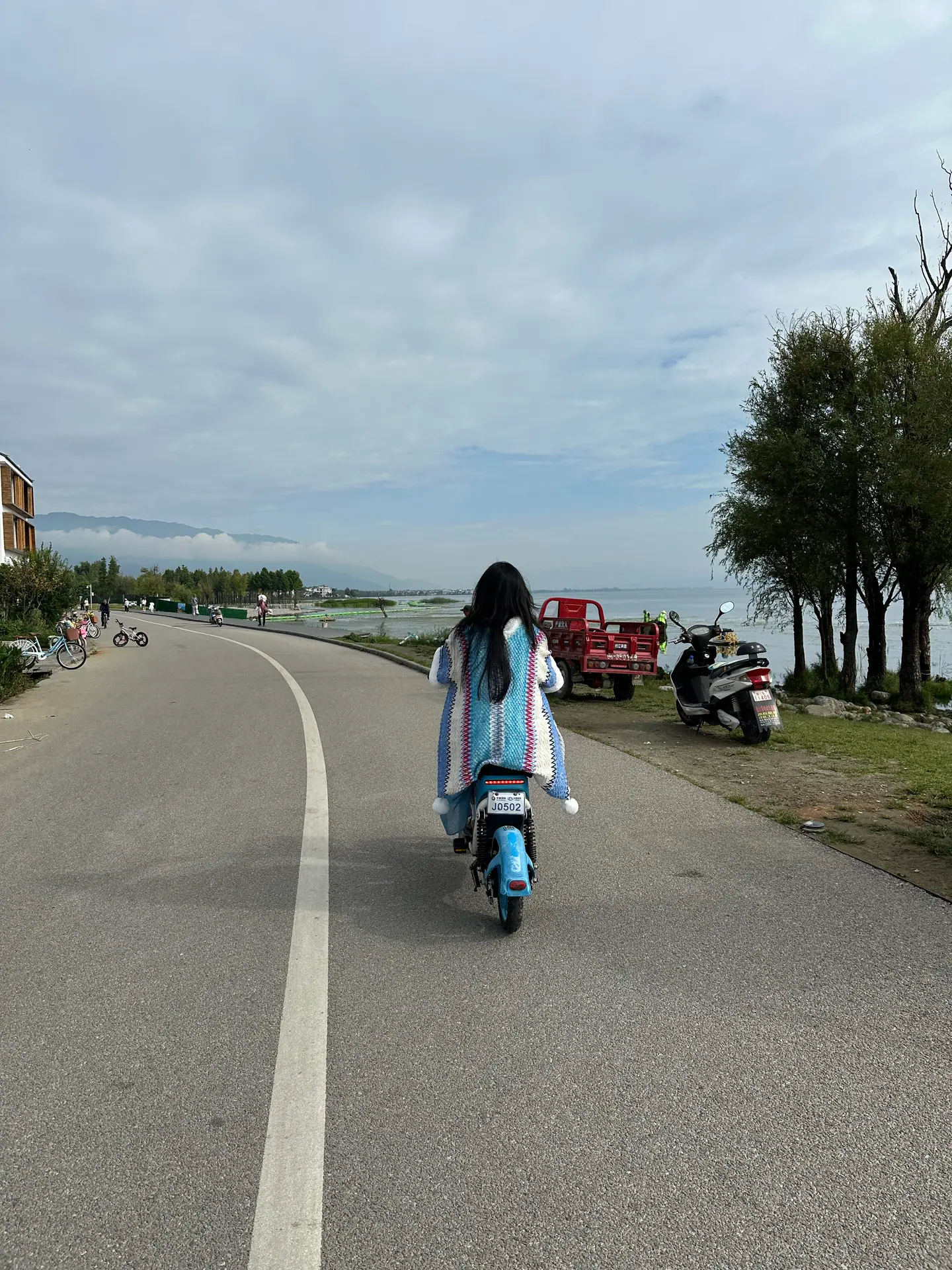 Viajera recorriendo en moto eléctrica la carretera que rodea el lago Erhai, Dali
