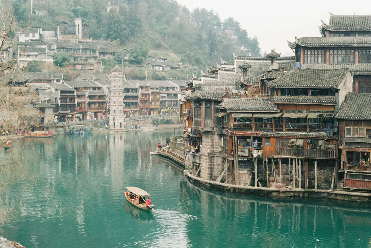 Casas de madera sobre pilotes a orillas del río Tuo en Fenghuang, con una barca