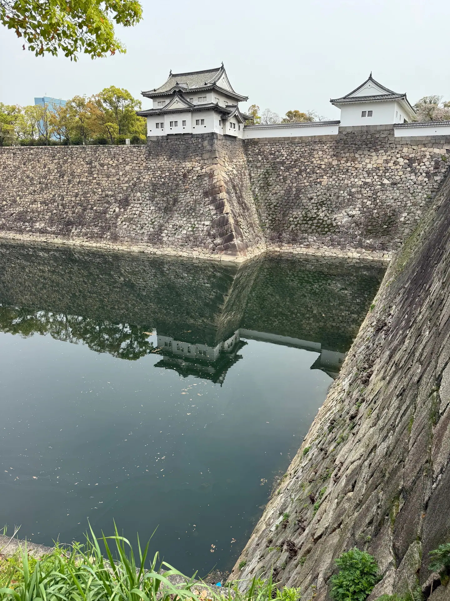 Foso con altas murallas de piedra y dos torretas blancas reflejadas en el agua, castillo de Osaka