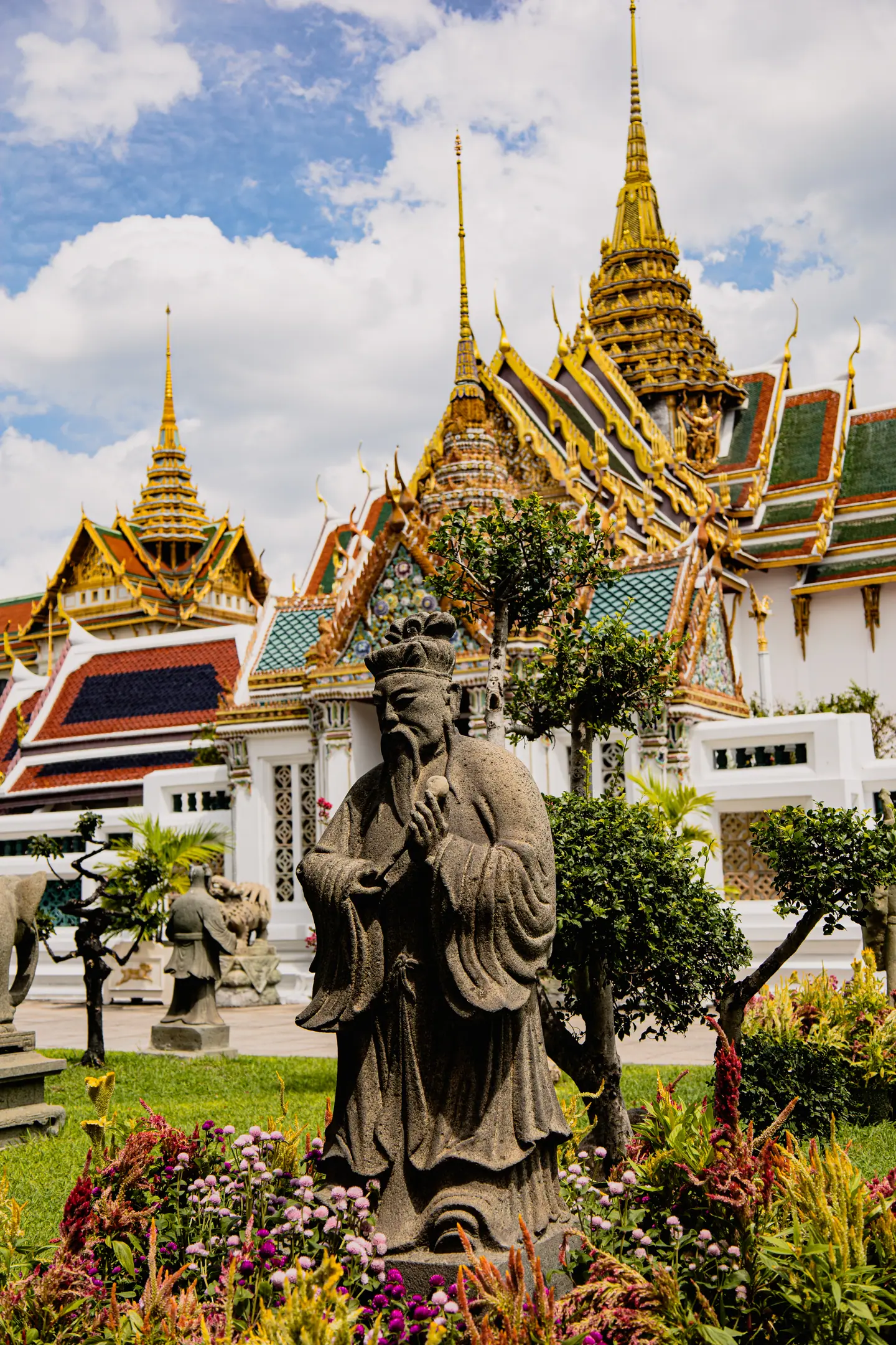 Tejados dorados del Gran Palacio de Bangkok con una estatua guardiana de piedra en el jardín