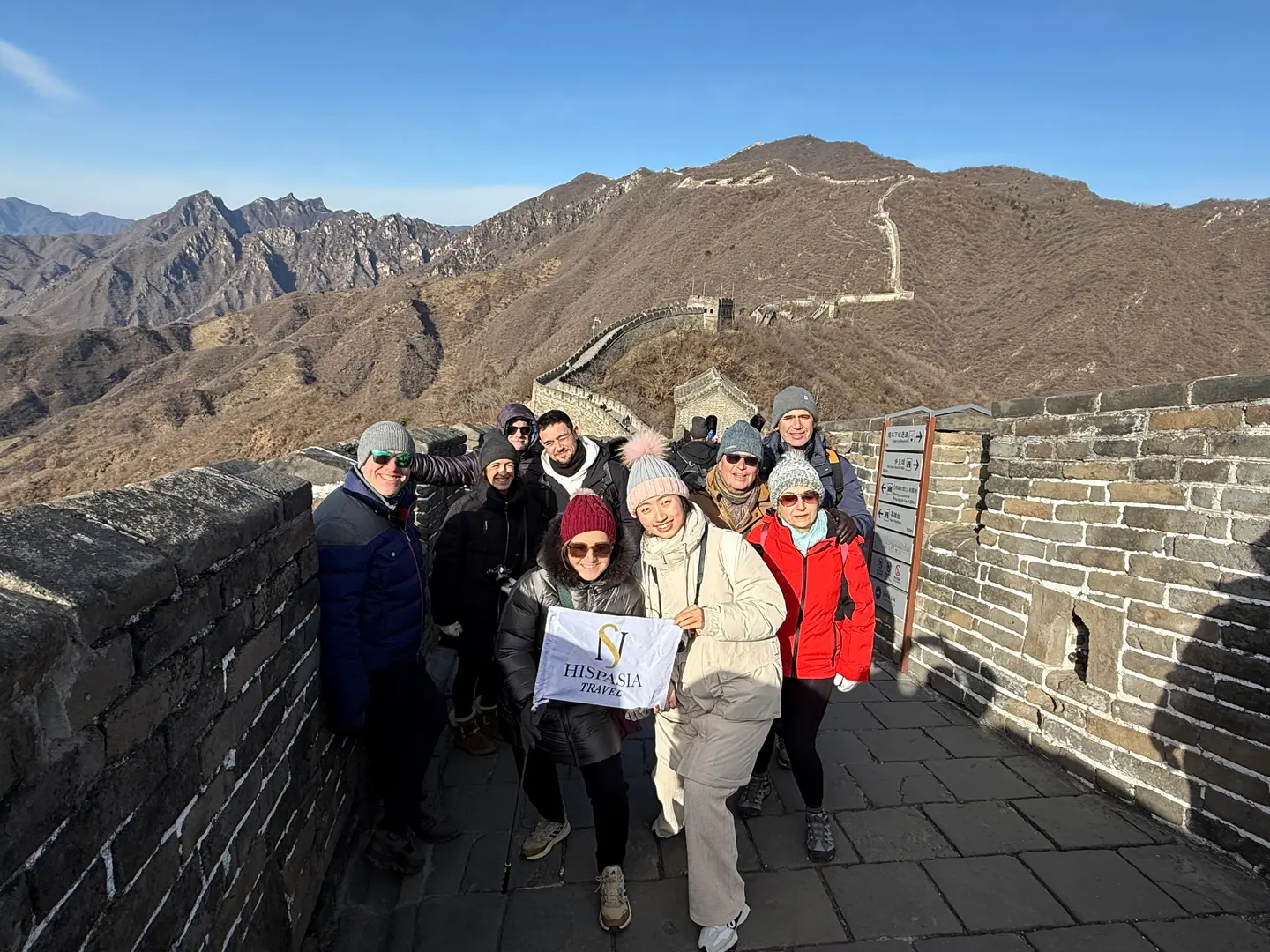 Grupo de viajeros sonriendo sobre la Gran Muralla con las montañas al fondo