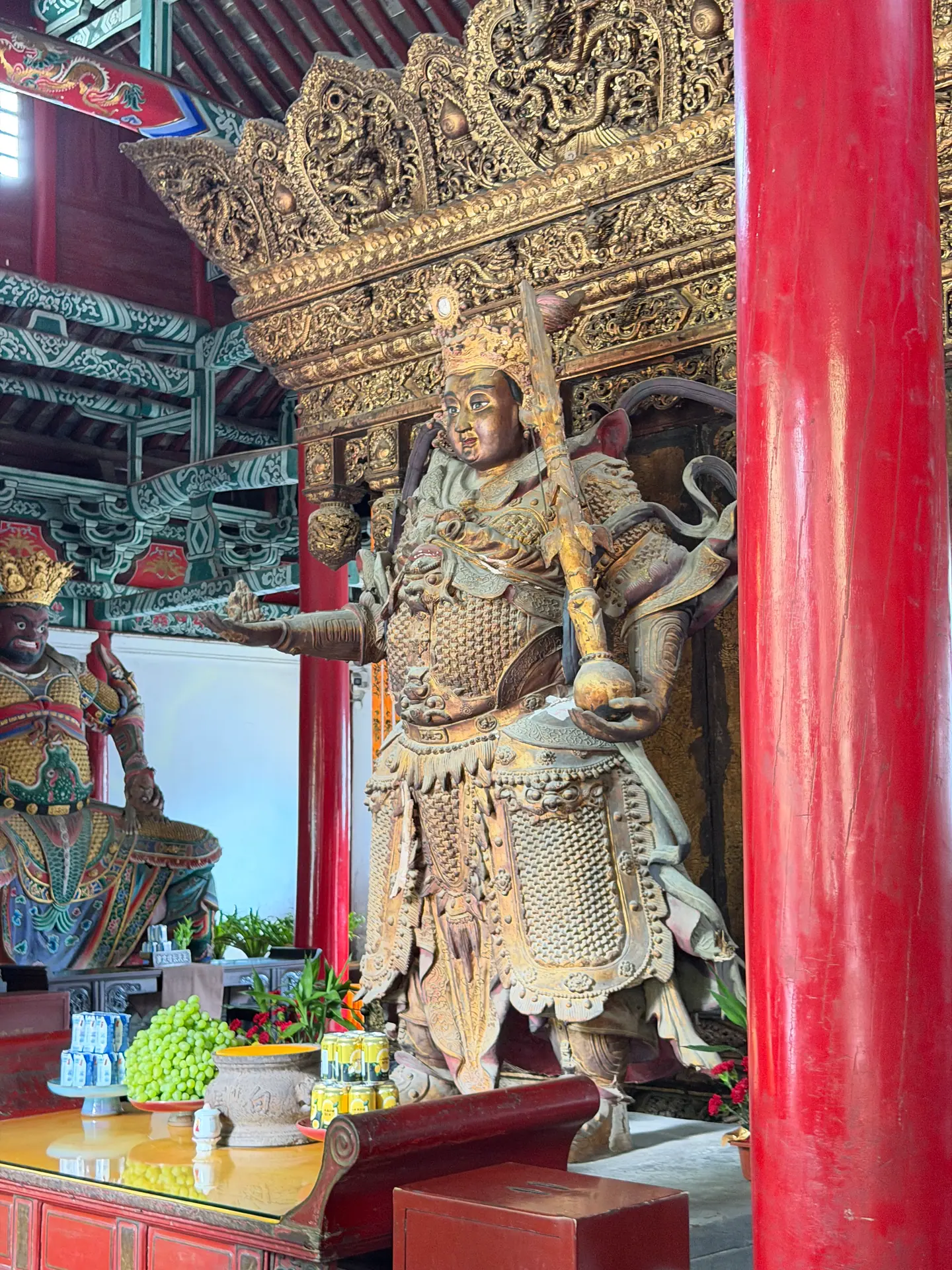 Estatua dorada de un rey celestial guardián entre columnas rojas del templo del Caballo Blanco