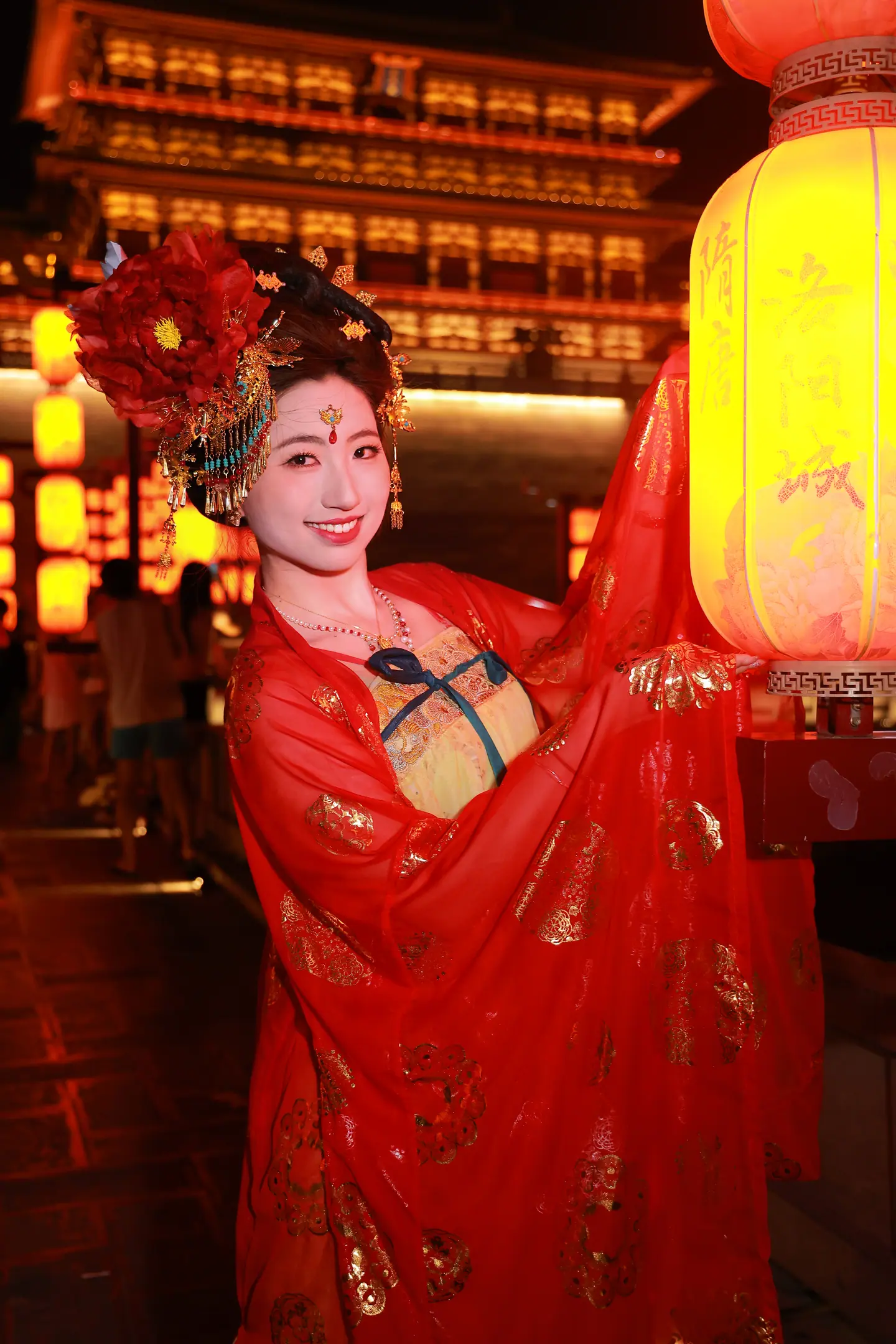 Modelo con Hanfu rojo y tocado floral junto a un gran farolillo en Luoyang de noche
