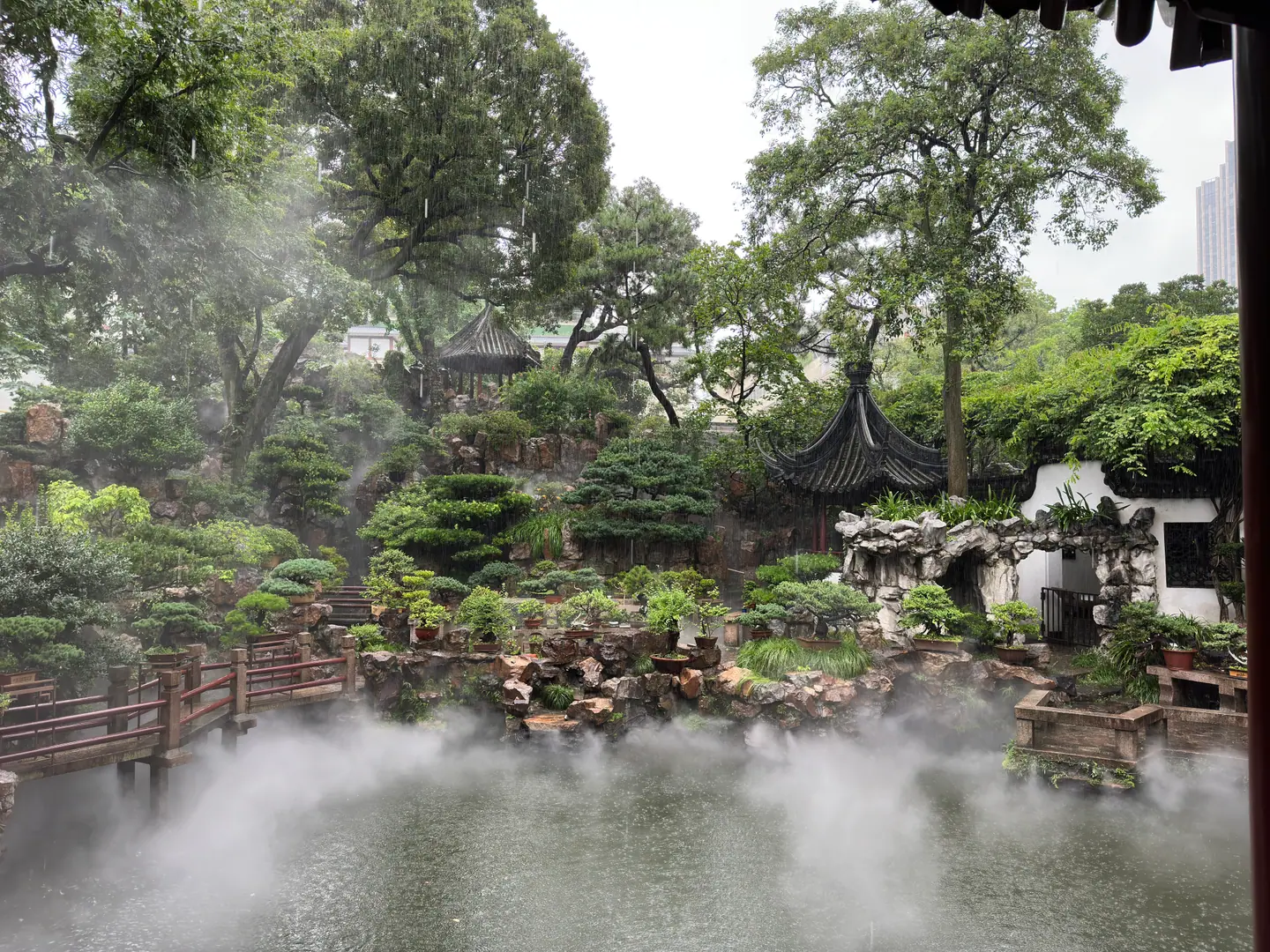 Estanque envuelto en bruma rodeado de rocas, pinos y pabellones en el Jardín Yuyuan, Shanghái
