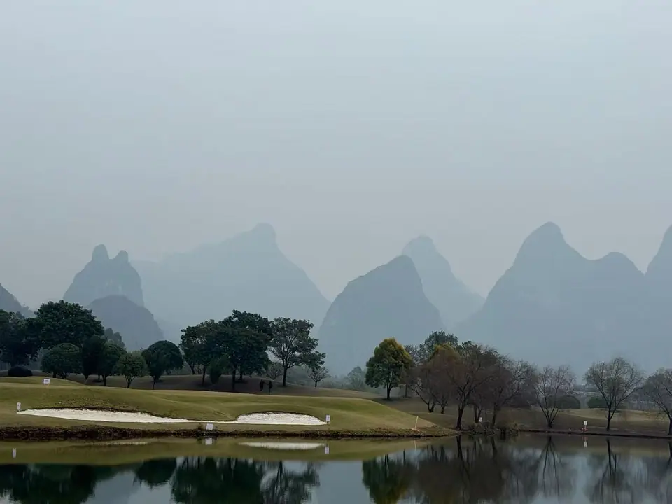 Picos kársticos envueltos en bruma junto a un estanque en Yangshuo