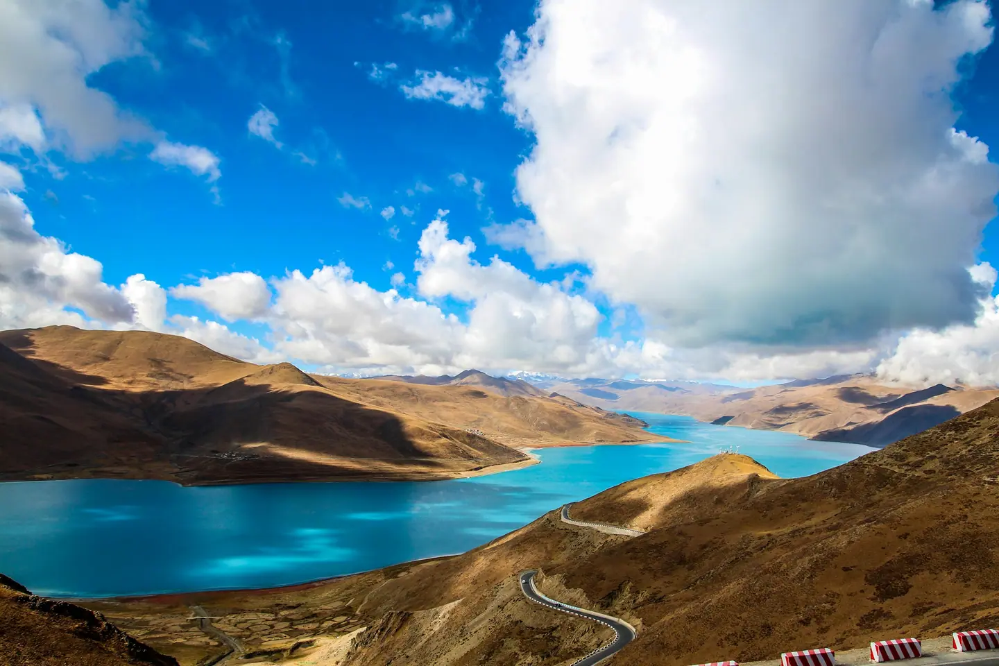 El lago Yamdrok, de color turquesa, serpenteando entre montañas pardas bajo un cielo azul con nubes