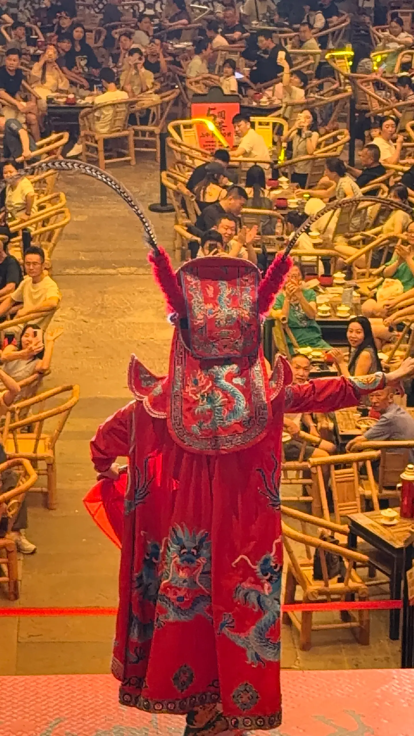 Actor de ópera de Sichuan con máscara roja y tocado de plumas entre el público