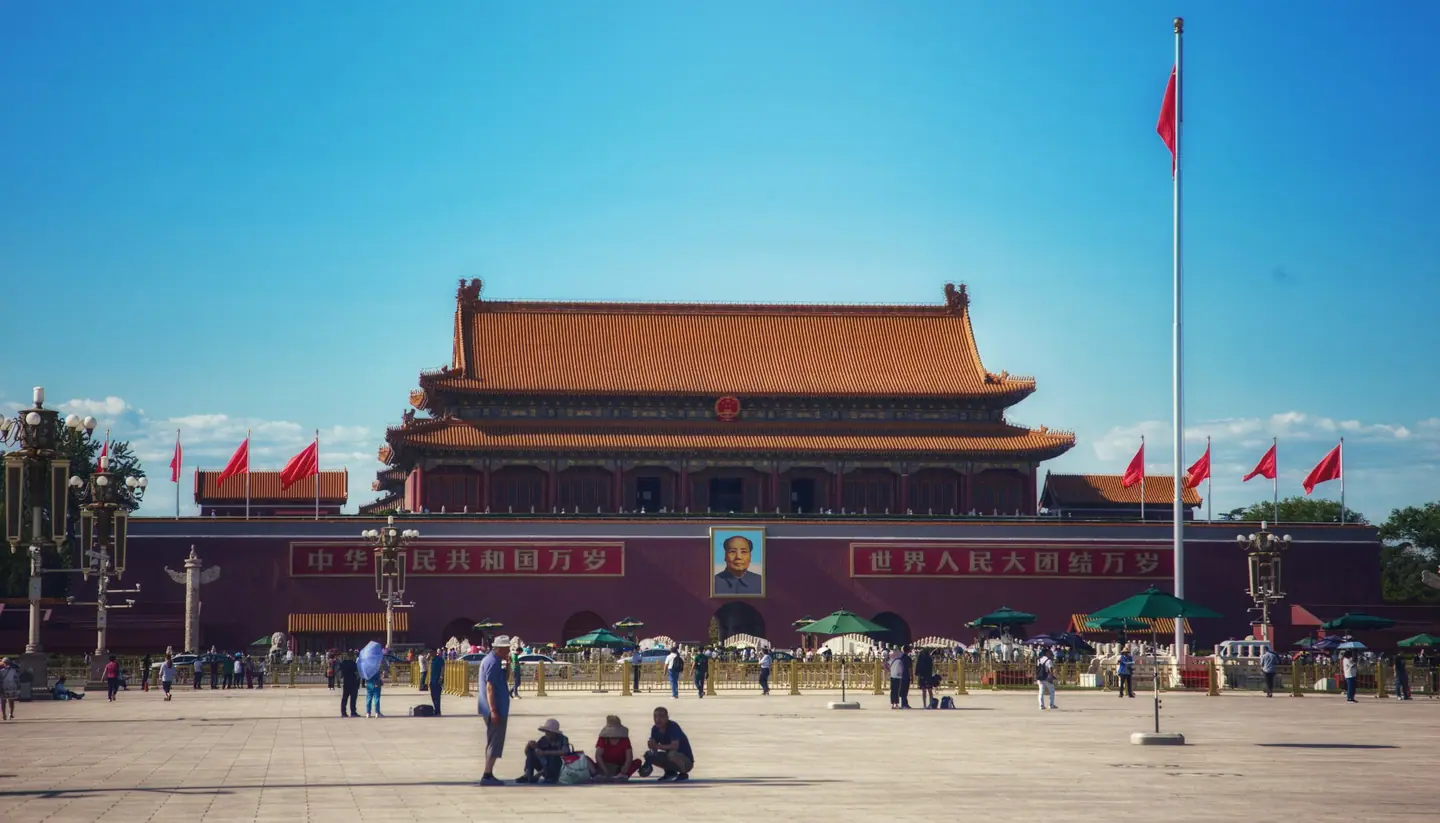 La Puerta de Tiananmén, con su retrato y sus banderas, al fondo de la plaza de Tiananmén bajo el cielo azul