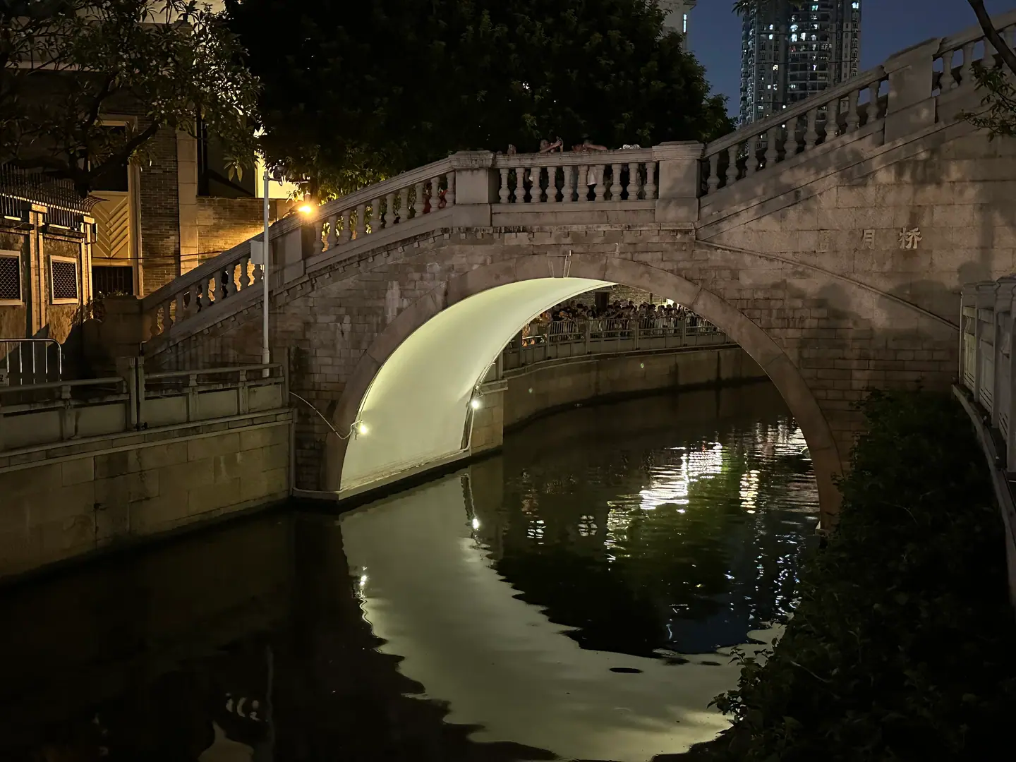 Puente de piedra en arco reflejado en el canal de Yong Qing Fang por la noche