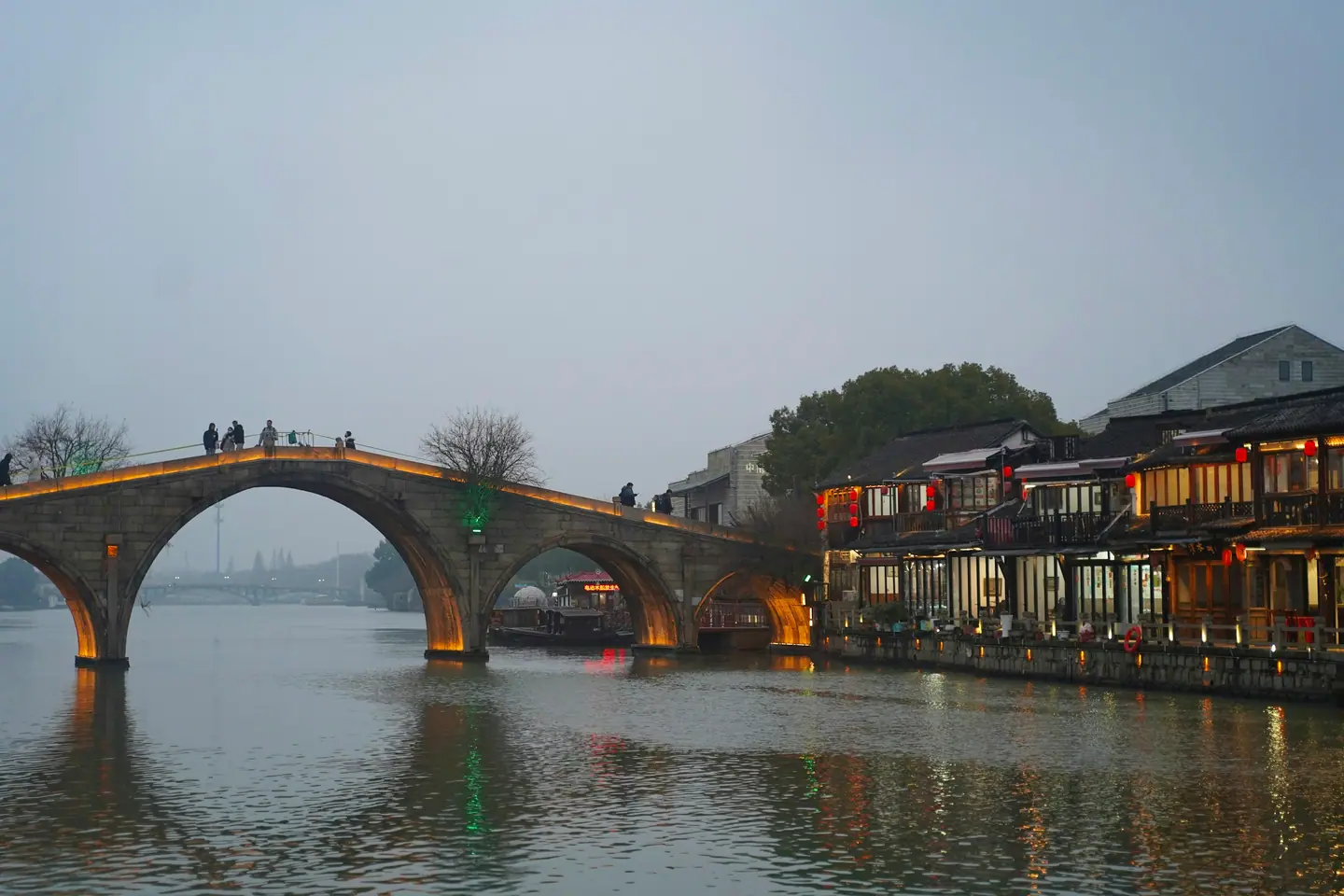 El puente de piedra de cinco arcos de Zhujiajiao al atardecer, con las casas iluminadas junto al agua