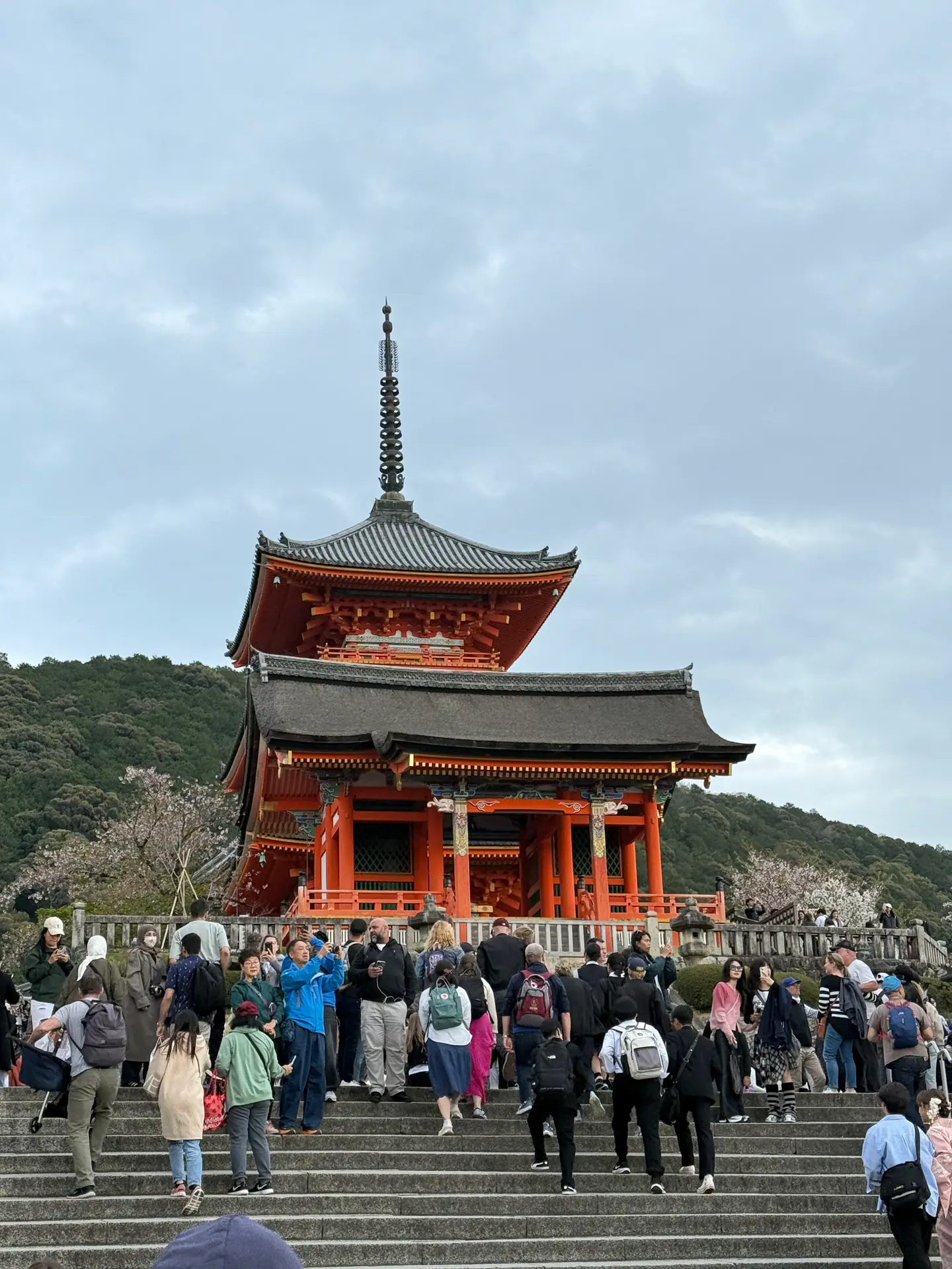 Visitantes subiendo la escalinata hacia una puerta bermellón y la pagoda de Kiyomizu-dera bajo cielo nublado, Kioto