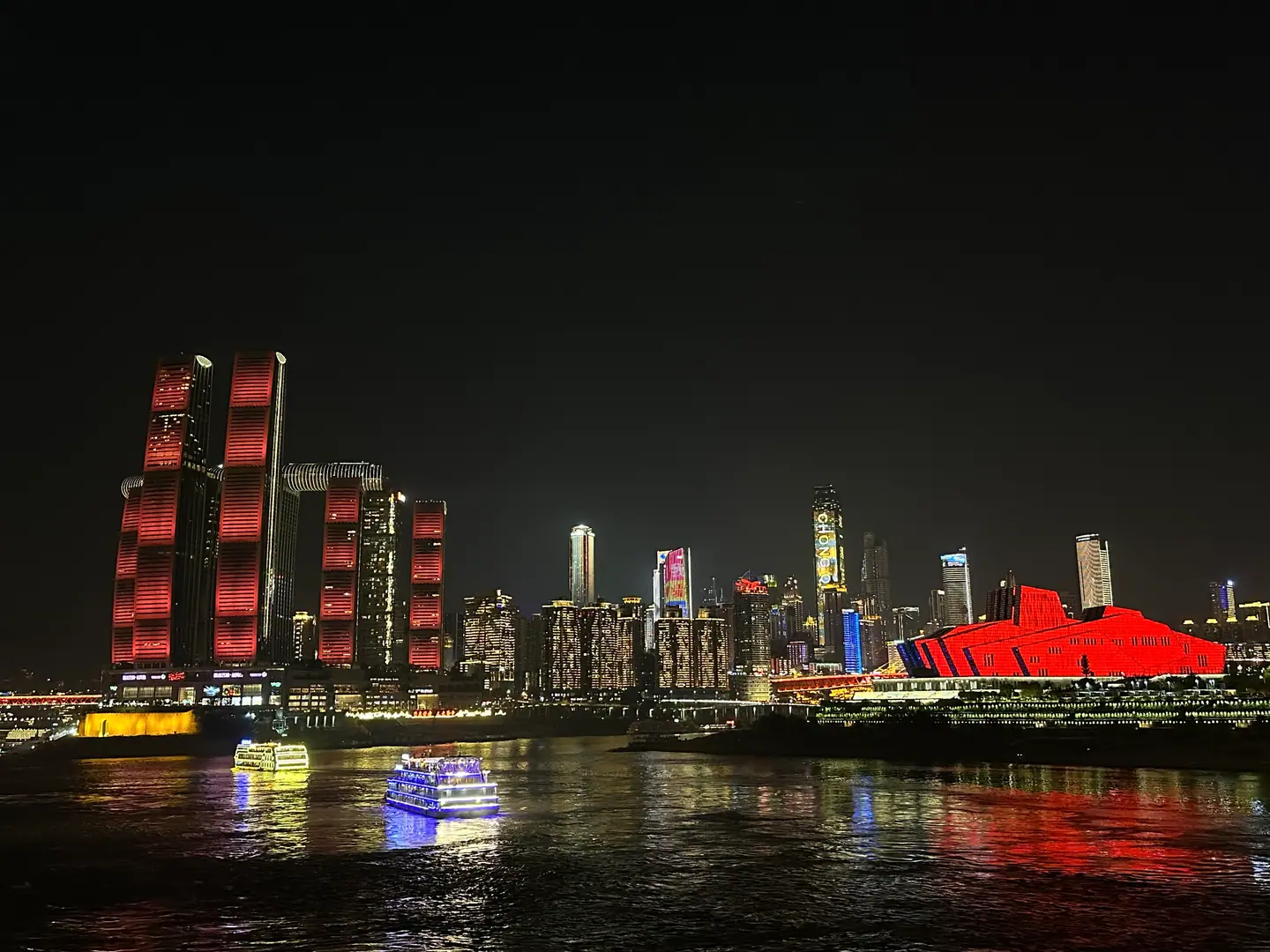 Raffles City iluminado en rojo y el Gran Teatro de Chongqing reflejados en el río de noche