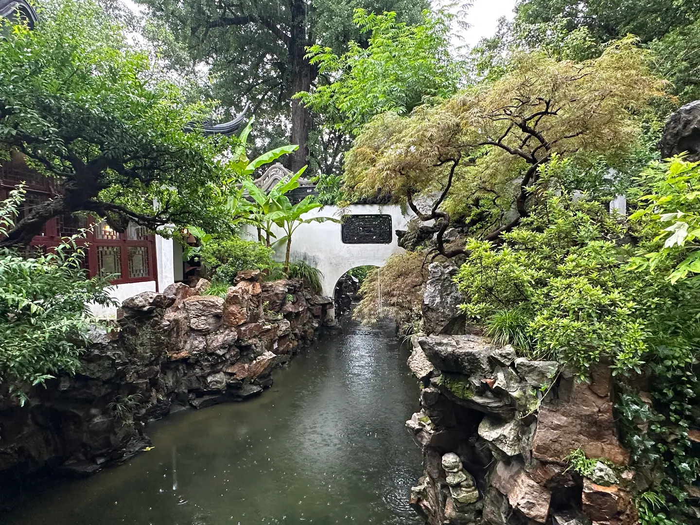 Canal entre rocallas y vegetación frondosa en el Jardín Yuyuan, Shanghái