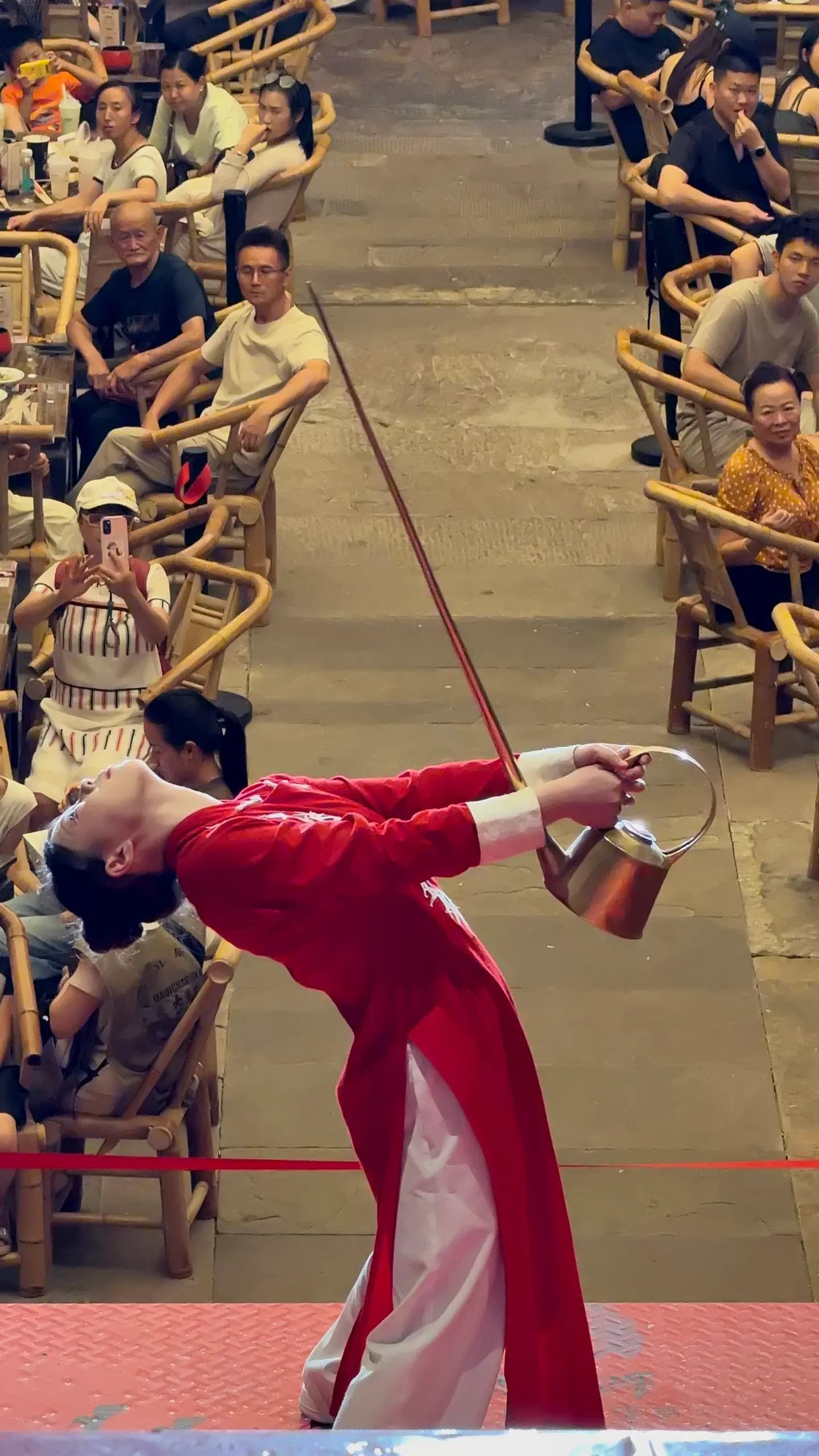 Artista de té en qipao rojo vertiendo té con una tetera de pico largo, Chongqing