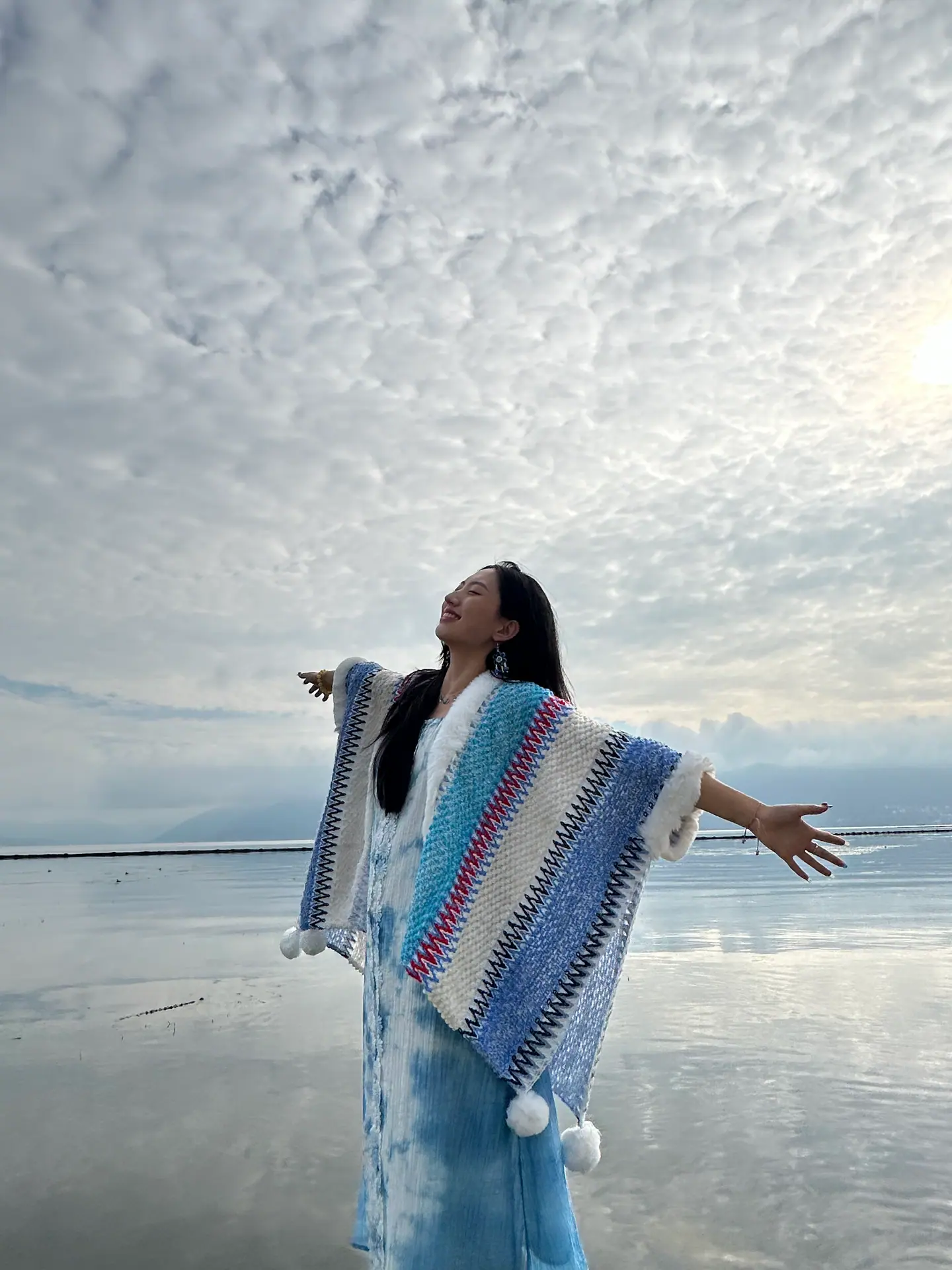 Viajera con poncho de colores con los brazos abiertos ante el lago Erhai, Dali